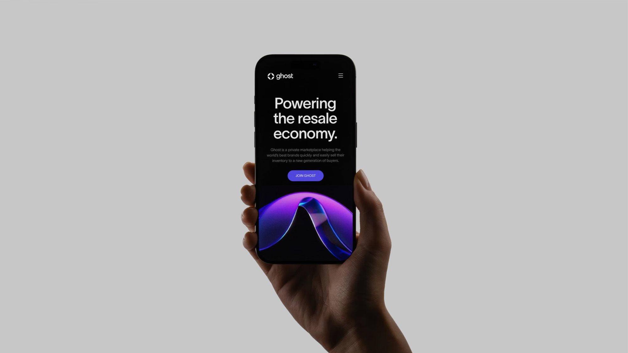 A hand holding an iPhone showing the Ghost mobile site: Powering the resale economy